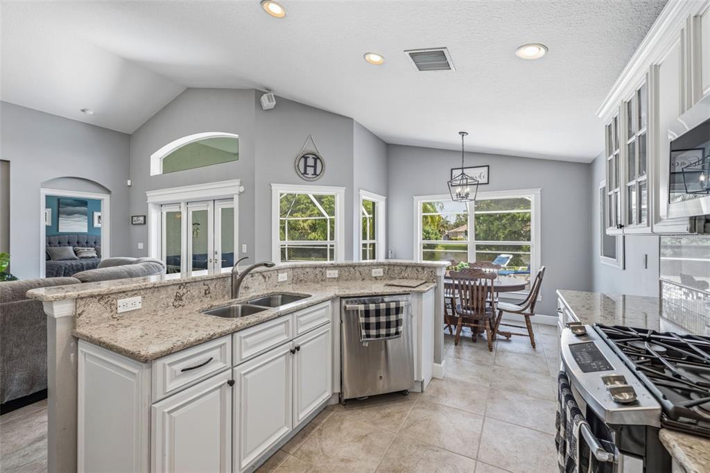 A kitchen with white cabinets, granite countertops, and stainless steel appliances overlooks a dining area — 10331 LIGHTNER BRIDGE DRIVE, TAMPA, FL