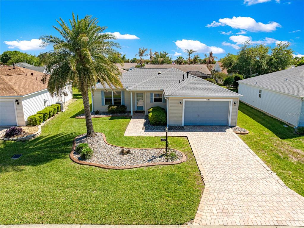 A single-story house with a light-colored exterior, a paved driveway, and a prominent palm tree — 2180 JASPER WAY, THE VILLAGES, FL