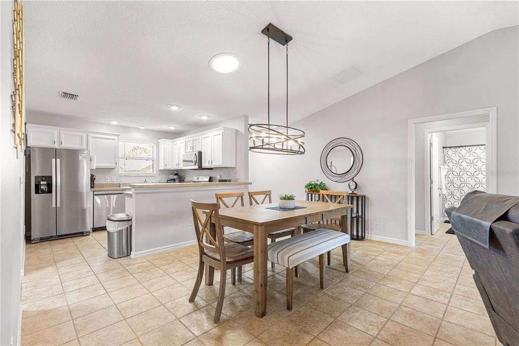A dining area with a wooden table and chairs sits adjacent to a white kitchen — 2180 JASPER WAY, THE VILLAGES, FL