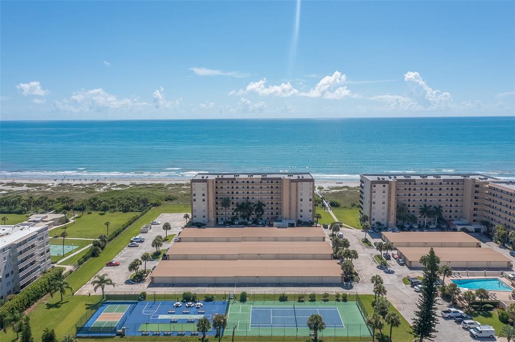 An aerial view shows two beachfront apartment buildings, parking lots, and tennis courts — 1890 N ATLANTIC AVENUE UNIT A302, COCOA BEACH, FL