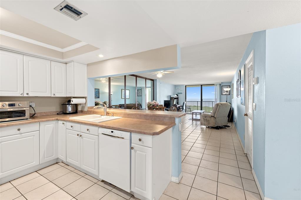 A kitchen with white cabinets and a breakfast bar overlooks a living area with ocean views — 1890 N ATLANTIC AVENUE UNIT A302, COCOA BEACH, FL