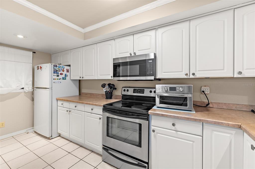 A kitchen features white cabinetry, stainless steel appliances, and light-colored countertops over tiled flooring — 1890 N ATLANTIC AVENUE UNIT A302, COCOA BEACH, FL