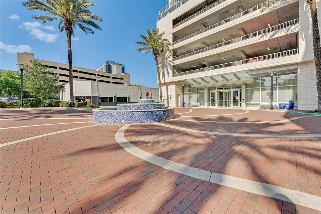 A brick plaza with a circular fountain sits in front of a modern high-rise building — 150 E ROBINSON STREET UNIT 2709, ORLANDO, FL