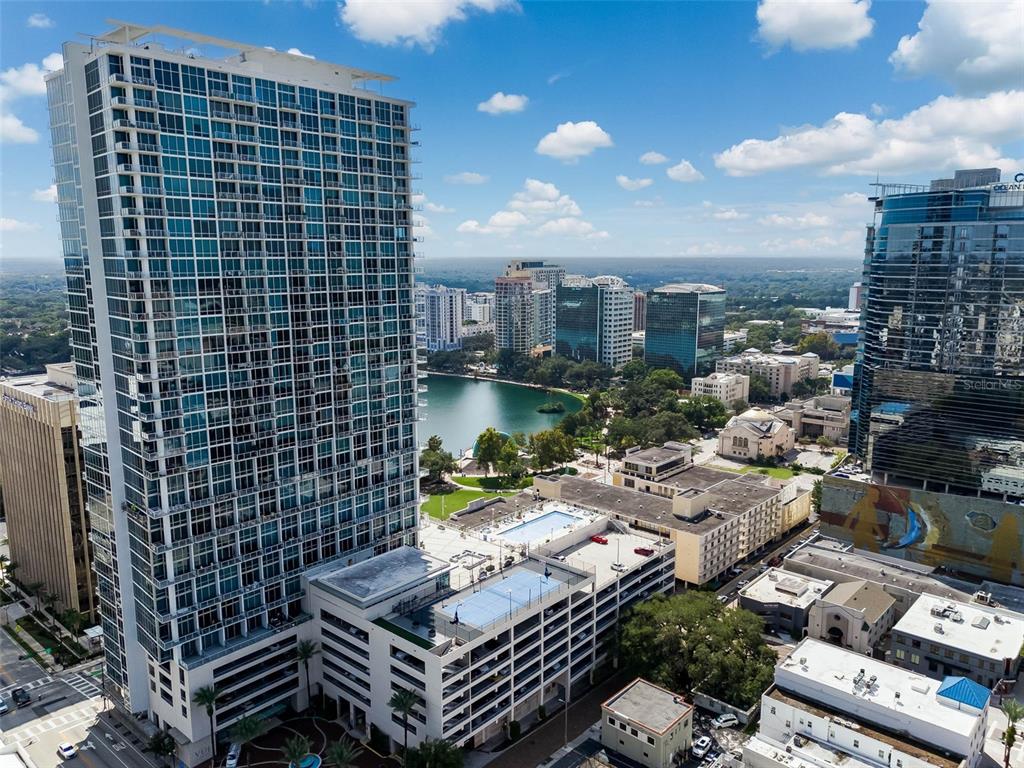 An aerial view of a tall residential skyscraper overlooking a lake and urban cityscape — 150 E ROBINSON STREET UNIT 2709, ORLANDO, FL