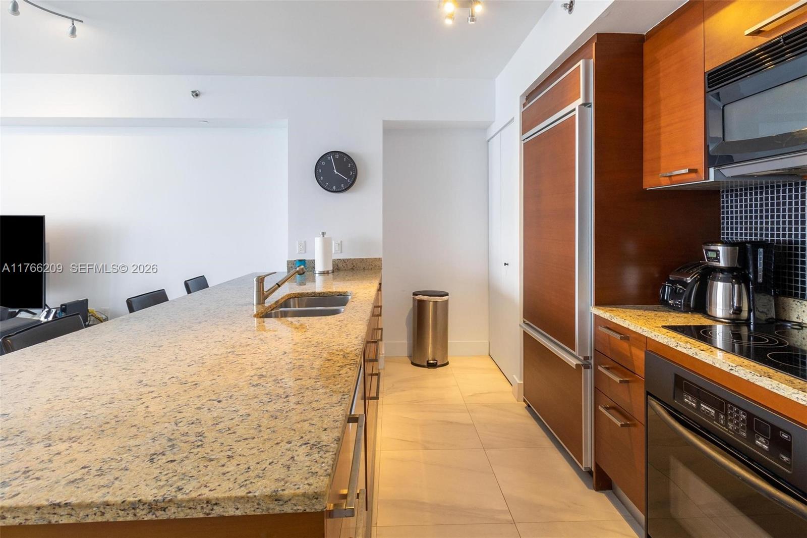 A modern kitchen features granite countertops, wood cabinetry, stainless steel appliances, and tile flooring — 1830 S OCEAN DR # 4705, Hallandale Beach FL 33009, HALLANDALE BEACH, FL
