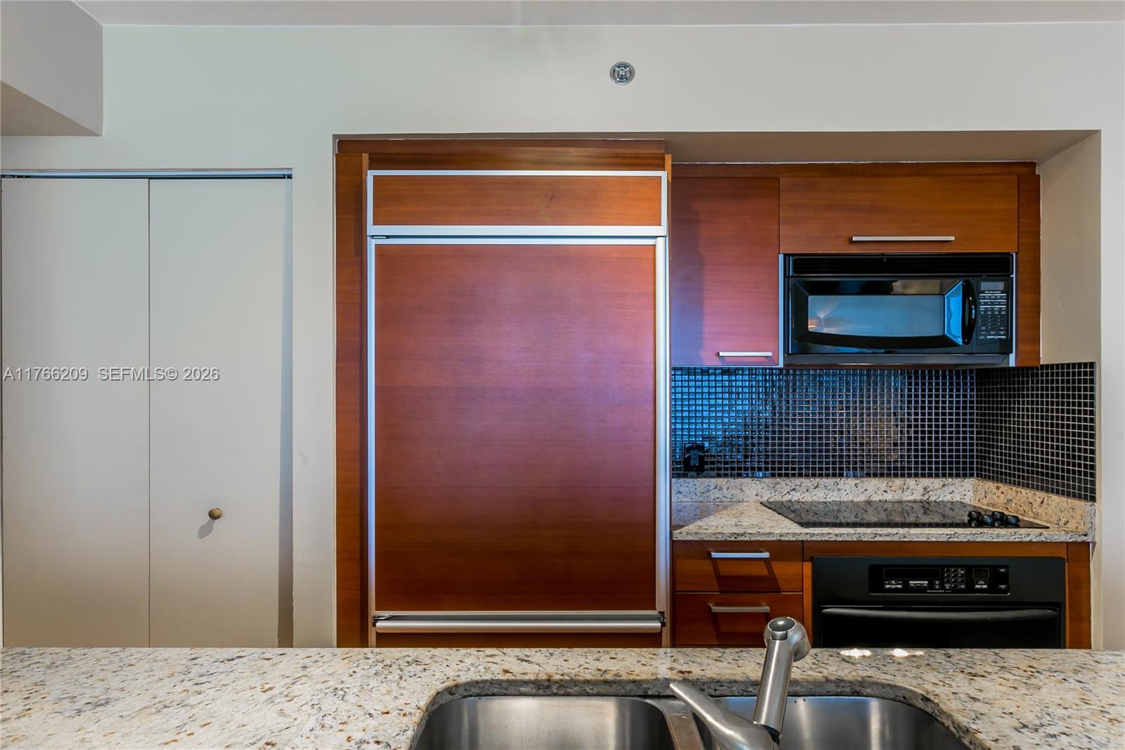 A kitchen features wood-paneled cabinetry, a built-in refrigerator, a black microwave, and granite countertops — 1830 S OCEAN DR # 4705, Hallandale Beach FL 33009, HALLANDALE BEACH, FL