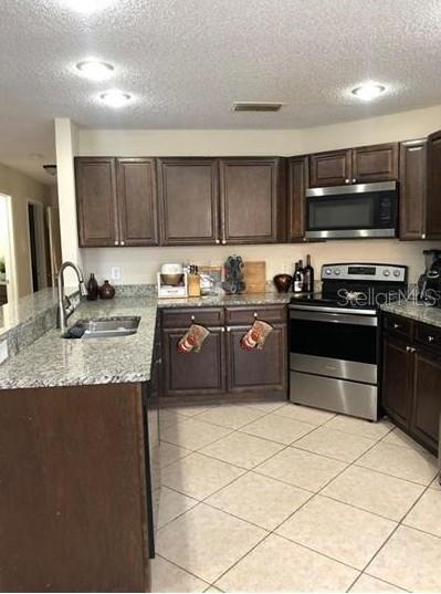 A kitchen features dark wood cabinets, granite countertops, stainless steel appliances, and tile flooring — 3211 BREWSTER DRIVE, KISSIMMEE, FL