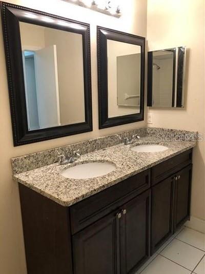 A double-sink bathroom vanity with dark wood cabinets, granite countertops, and two framed mirrors — 3211 BREWSTER DRIVE, KISSIMMEE, FL