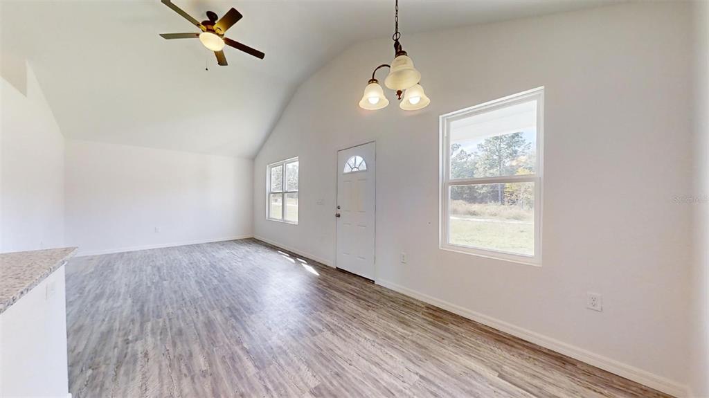 An empty room with vaulted ceilings, wood-look flooring, a ceiling fan, and a chandelier — 13730 SW 111TH STREET, DUNNELLON, FL