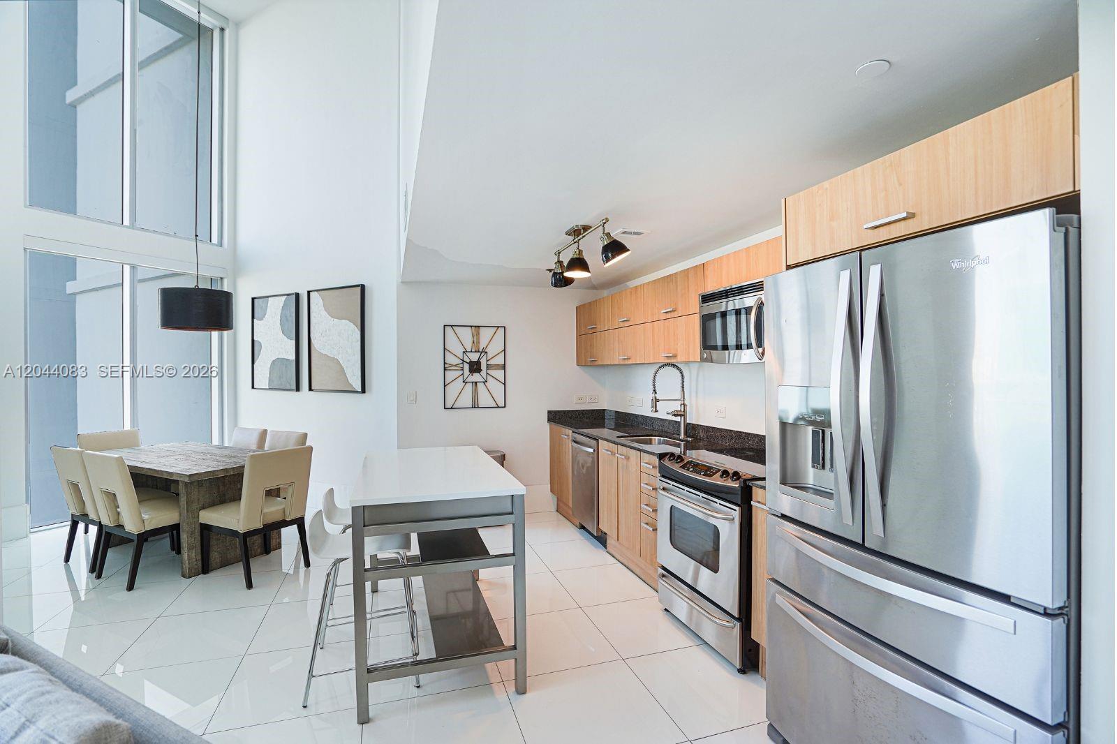 A modern kitchen with light wood cabinets, stainless steel appliances, and a dining area nearby — 350 S Miami Ave # 713, Miami FL 33130, MIAMI, FL