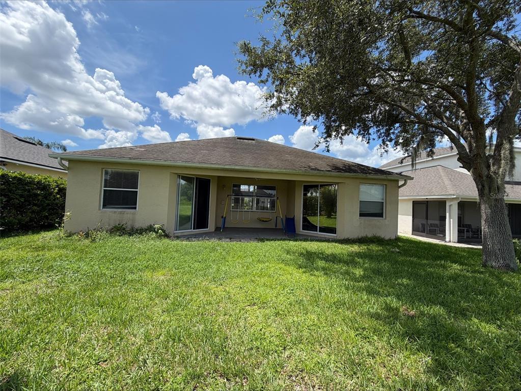 The backyard features a tan stucco house with a covered patio and a large tree — 3511 MAPLE RIDGE LOOP, KISSIMMEE, FL