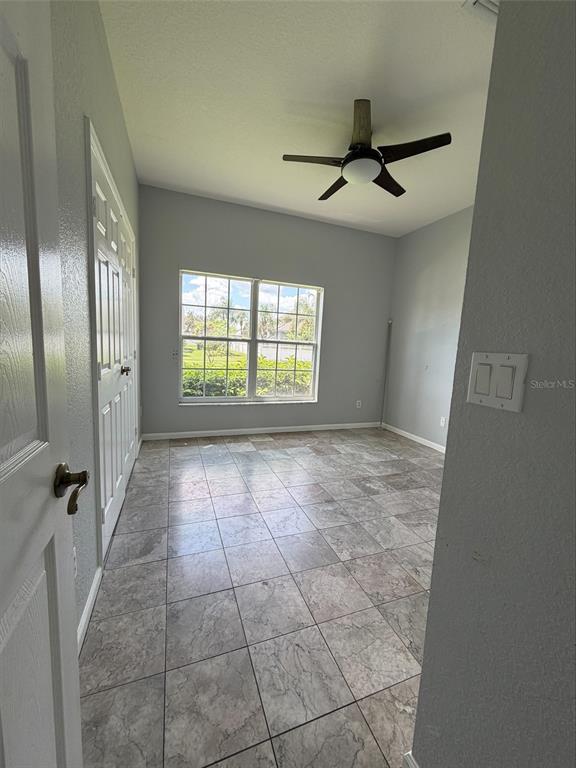 An empty room with gray walls, tile flooring, a ceiling fan, and a large window — 3511 MAPLE RIDGE LOOP, KISSIMMEE, FL