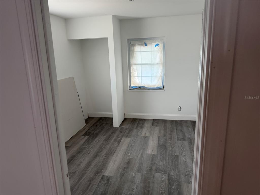 An interior view of a room with gray wood-look flooring and a window covered in plastic — 6044 SE AGNEW ROAD, BELLEVIEW, FL