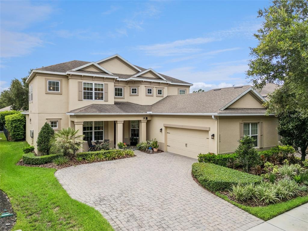 A two-story beige house with a paved driveway, a two-car garage, and landscaped front gardens — 7773 MINUTEMEN LOOP, WINTER GARDEN, FL