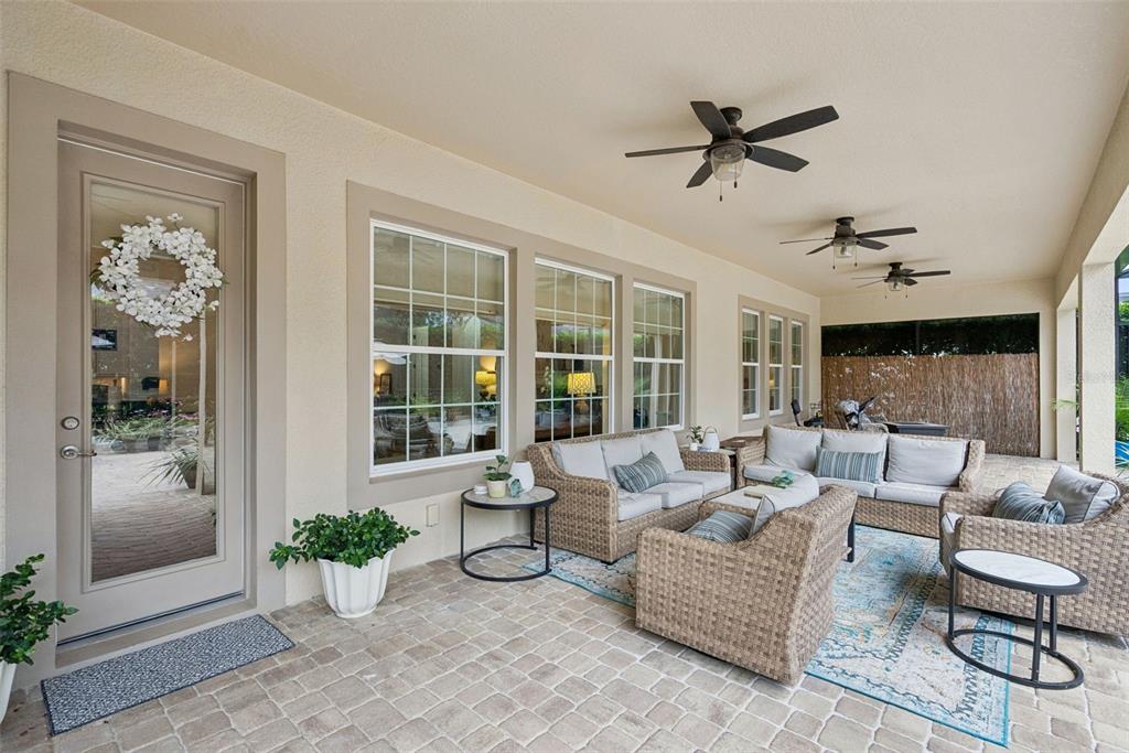 A covered patio features wicker furniture, ceiling fans, and a stone-tiled floor — 7773 MINUTEMEN LOOP, WINTER GARDEN, FL