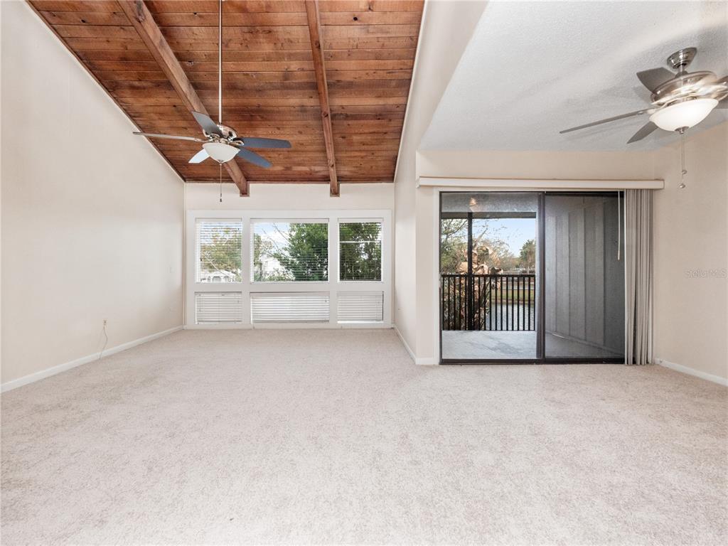 A living room features a vaulted wood-plank ceiling, beige carpeting, and a sliding glass door — 5789 PEREGRINE AVENUE UNIT 30-C10-2, ORLANDO, FL