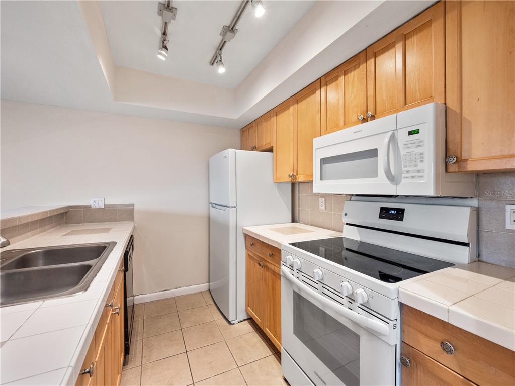 A kitchen features light wood cabinets, white appliances, tiled countertops, and a double basin sink — 5789 PEREGRINE AVENUE UNIT 30-C10-2, ORLANDO, FL