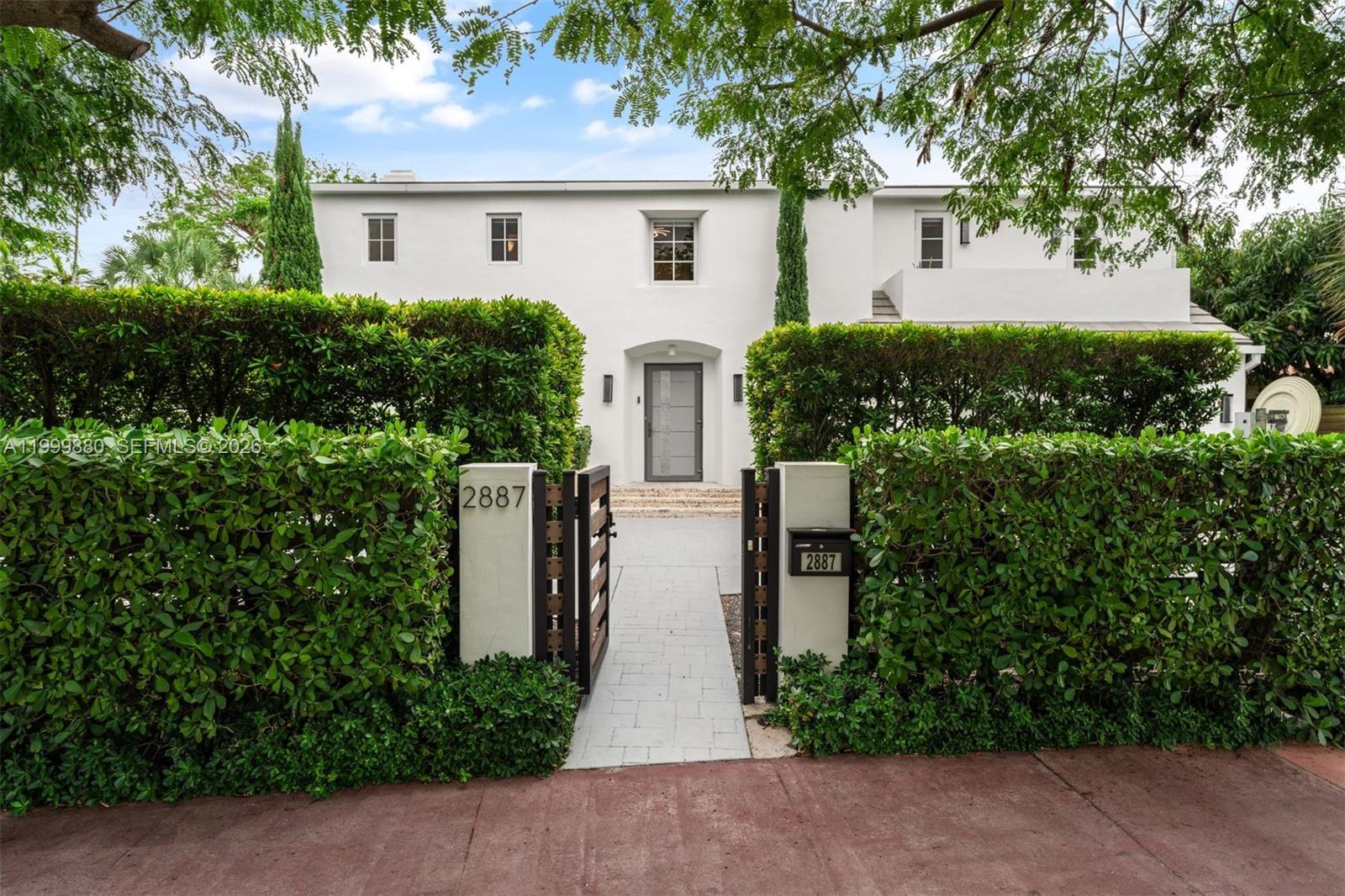 A white two-story house is viewed from the street behind a tall green hedge — 2887 Pine Tree Dr, Miami Beach FL 33140, MIAMI BEACH, FL