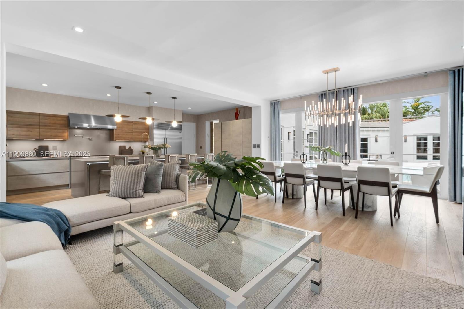 An open-concept living and dining area features a modern kitchen, glass coffee table, and chandelier — 2887 Pine Tree Dr, Miami Beach FL 33140, MIAMI BEACH, FL