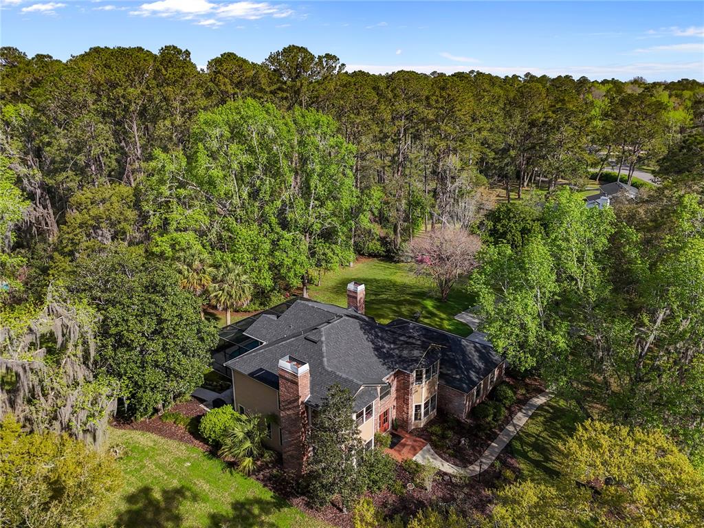 An aerial view shows a two-story house with a dark roof surrounded by dense trees — 1118 SW 112TH STREET, GAINESVILLE, FL