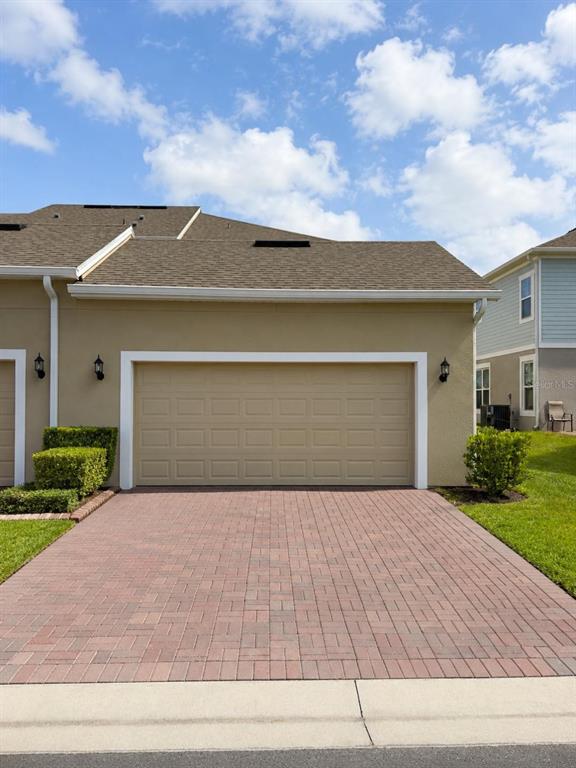 A tan townhome exterior features a two-car garage and a red brick paver driveway — 7030 TWILIGHT BAY DRIVE, WINTER GARDEN, FL