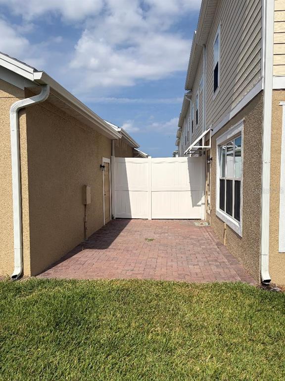 A paved patio area sits between two tan exterior walls with a white privacy gate — 7030 TWILIGHT BAY DRIVE, WINTER GARDEN, FL