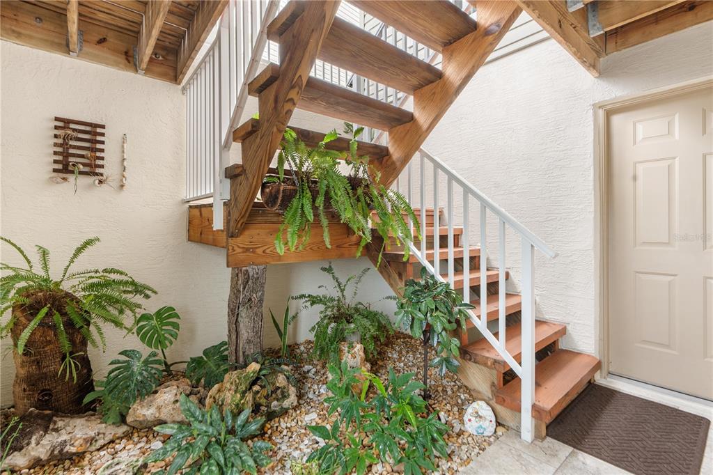 A wooden staircase with white railings sits above a gravel garden with potted plants — 8250 AQUILA STREET, PORT RICHEY, FL