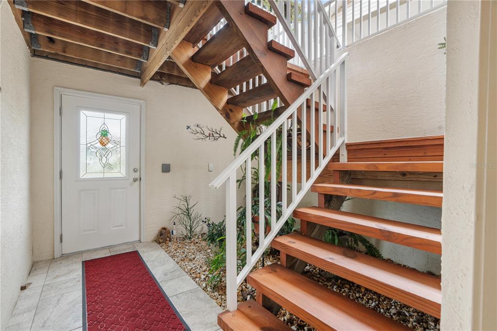 An entryway features a white door, a red rug, and wooden stairs with white railings — 8250 AQUILA STREET, PORT RICHEY, FL