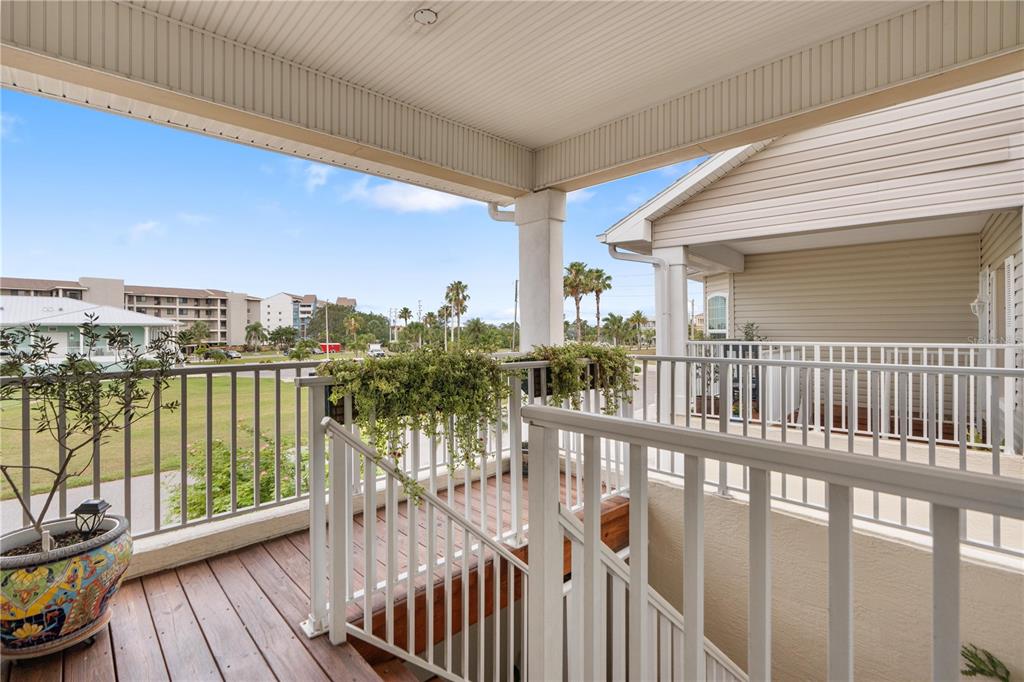 A covered wooden balcony with white railings overlooks a grassy area and nearby buildings — 8250 AQUILA STREET, PORT RICHEY, FL