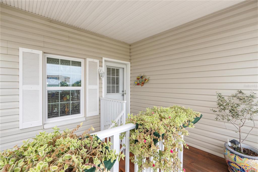 A covered porch features beige vinyl siding, a white railing with hanging plants, and a door — 8250 AQUILA STREET, PORT RICHEY, FL