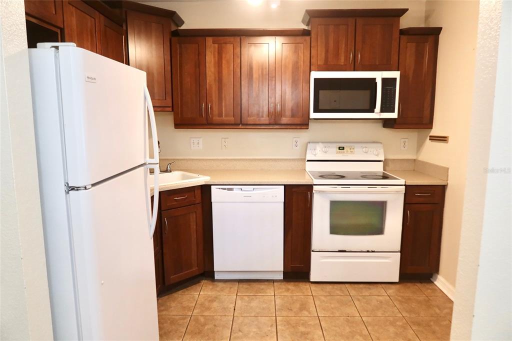 A kitchen features dark wood cabinets, white appliances, and tan tile flooring — 2704 NW 1ST AVENUE, GAINESVILLE, FL