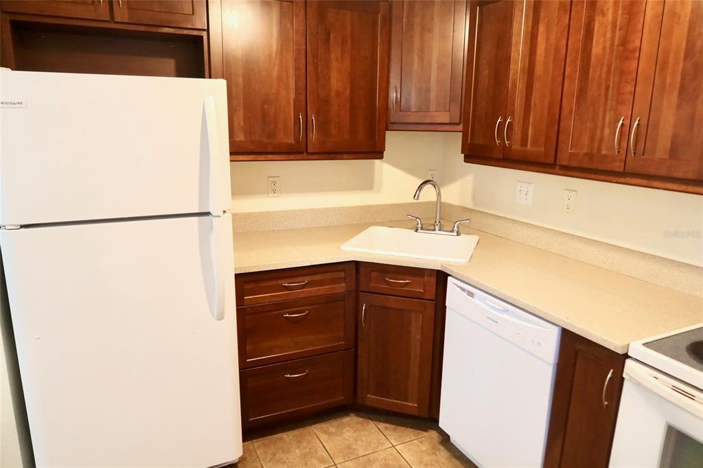 A kitchen features dark wood cabinets, white appliances, and a corner sink with beige countertops — 2704 NW 1ST AVENUE, GAINESVILLE, FL