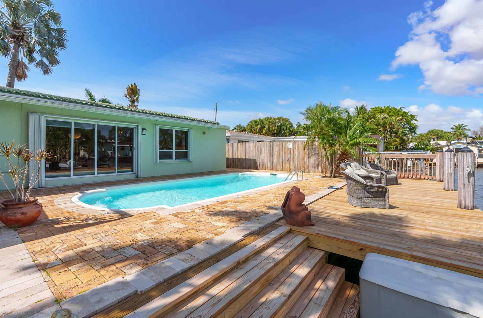 A backyard features a swimming pool, a wooden deck, and a patio next to a house — 101 SE 14th Street, Pompano Beach FL 33060, POMPANO BEACH, FL