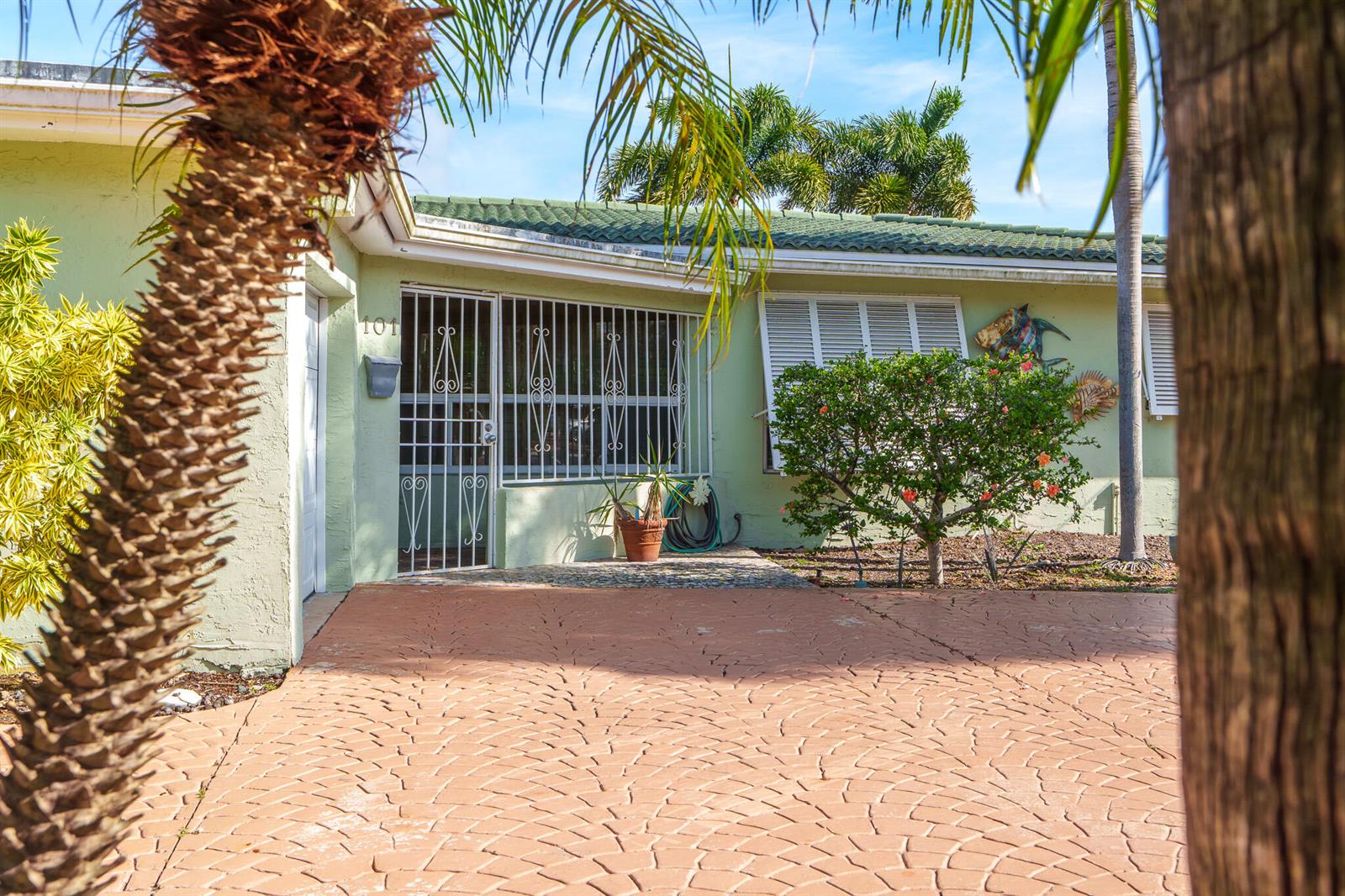 A light green house with a patterned driveway, security bars on the door, and landscaping — 101 SE 14th Street, Pompano Beach FL 33060, POMPANO BEACH, FL