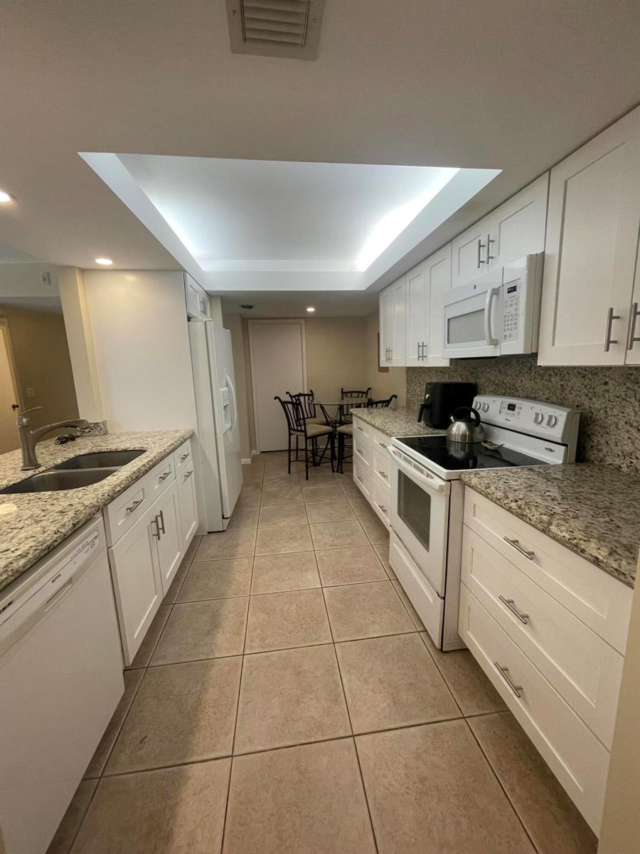 A galley kitchen features white cabinets, granite countertops, tile flooring, and stainless steel appliances — 450 Egret Circle # 9203, Delray Beach FL 33444, DELRAY BEACH, FL