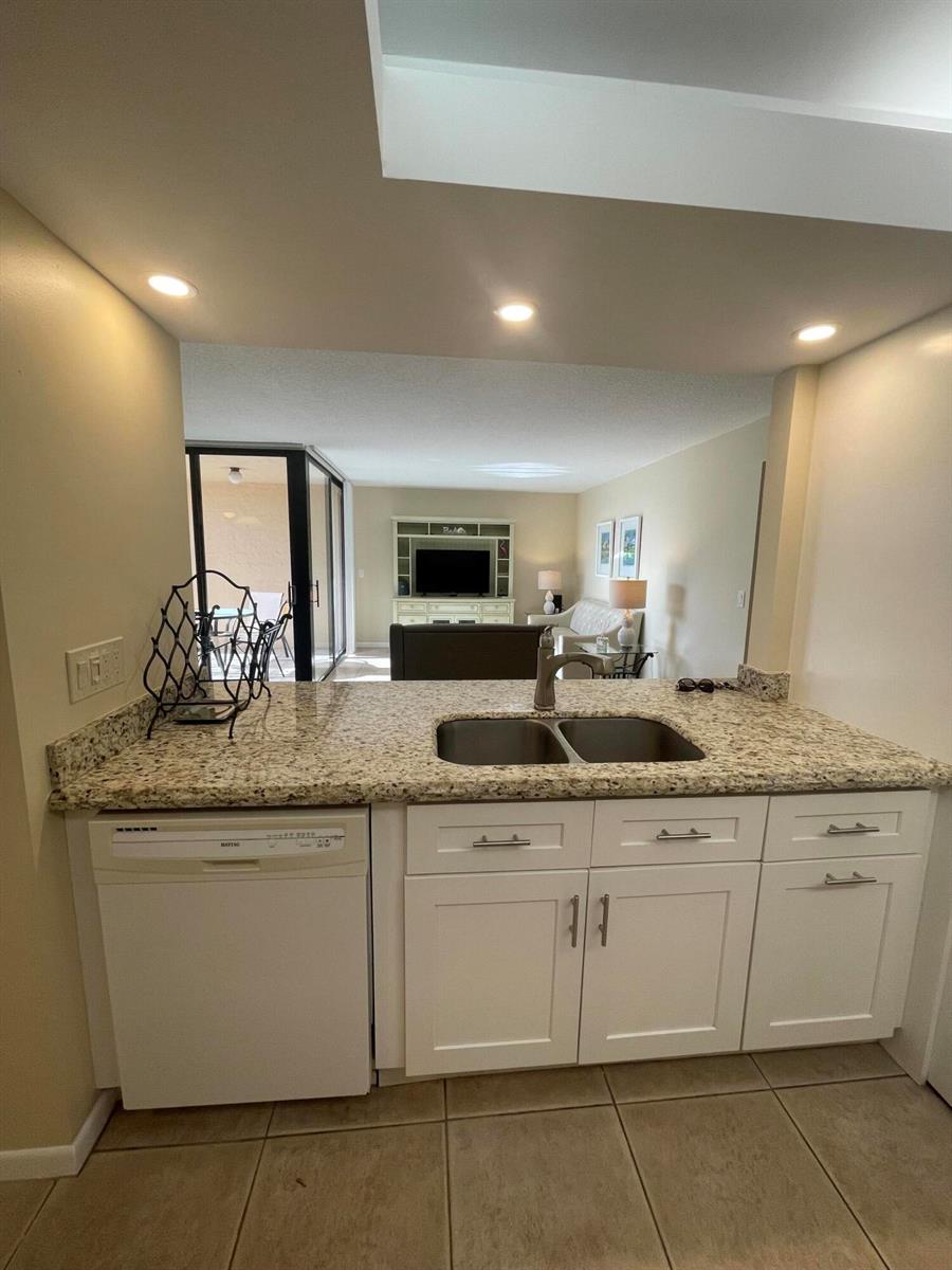 A kitchen peninsula with granite countertops and white cabinets overlooks a living room area — 450 Egret Circle # 9203, Delray Beach FL 33444, DELRAY BEACH, FL