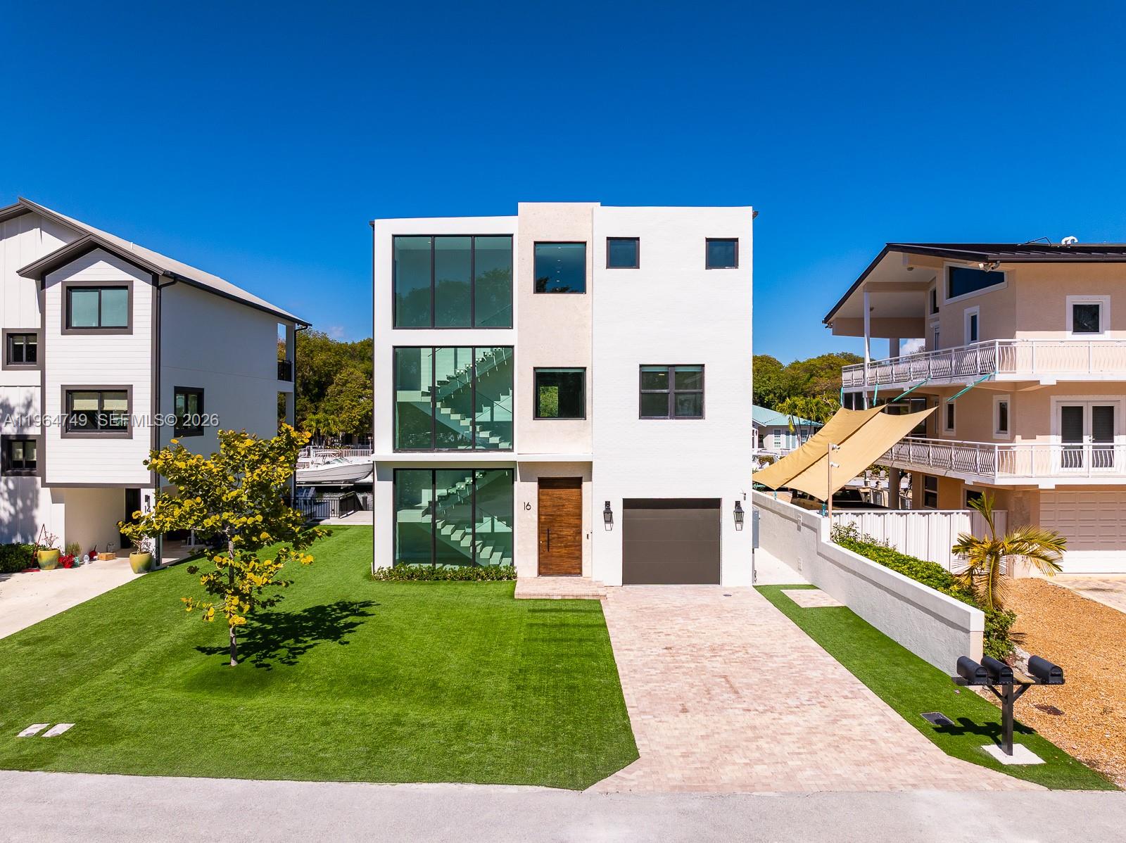 A modern three-story white house with a glass staircase, garage, and front lawn — 16 Bass Ave, Key Largo FL 33037, KEY LARGO, FL
