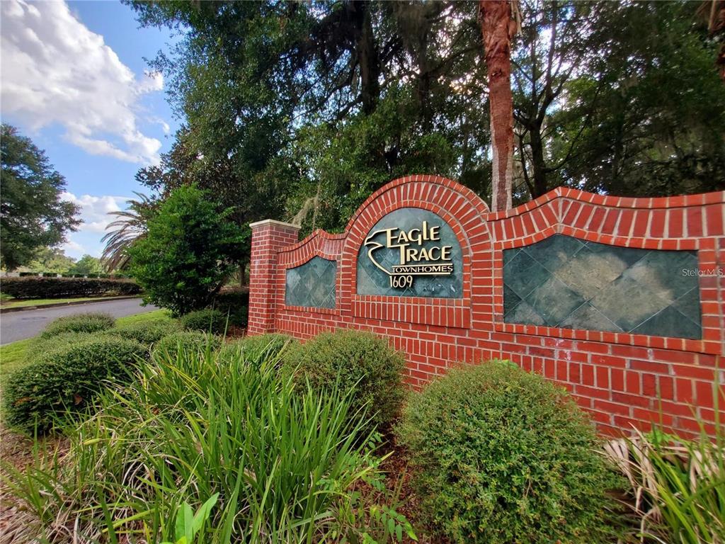 A brick entrance sign for Eagle Trace Townhomes stands surrounded by green landscaping and trees — 1561 NW 29TH ROAD UNIT 8, GAINESVILLE, FL