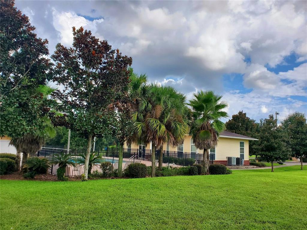 A yellow building with a fenced pool area is surrounded by trees and green grass — 1561 NW 29TH ROAD UNIT 8, GAINESVILLE, FL