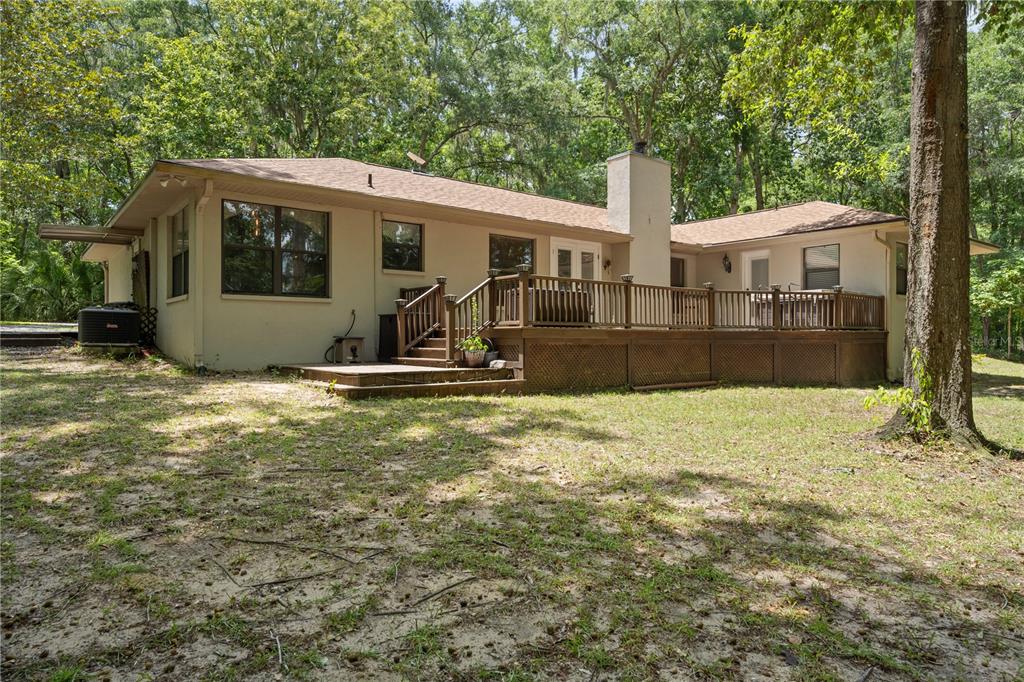 The rear exterior of a single-story house features a large wooden deck and chimney — 18451 NW 141ST AVENUE, WILLISTON, FL