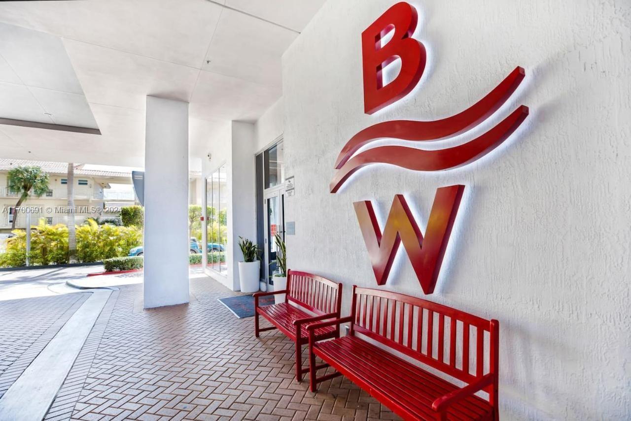 Two red wooden benches sit on a brick walkway beneath a large red BW logo — 2602 E Hallandale Beach Blvd # R508, Hallandale Beach FL 33009, HALLANDALE BEACH, FL