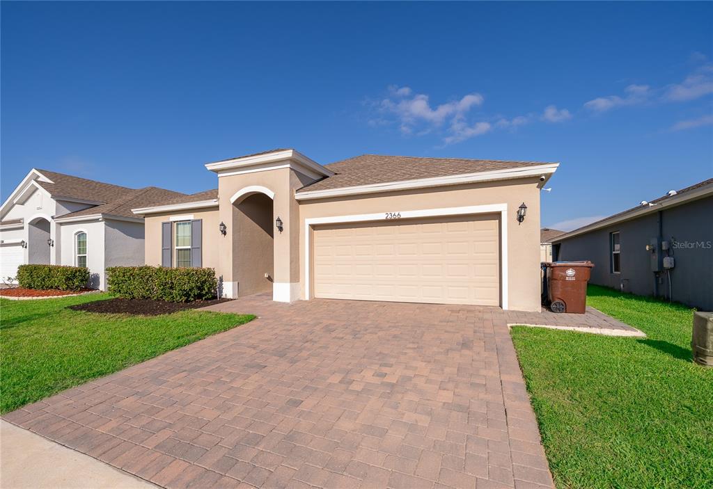 A single-story house features a tan stucco exterior, a two-car garage, and a paver driveway — 2366 WHITE CEDAR WAY, HAINES CITY, FL