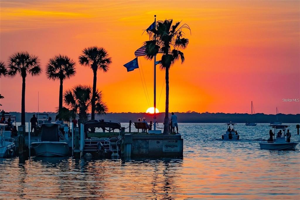 A sunset view over a harbor with boats, palm trees, and a flag-topped pier — 16178 TRADING POST ROAD, PUNTA GORDA, FL