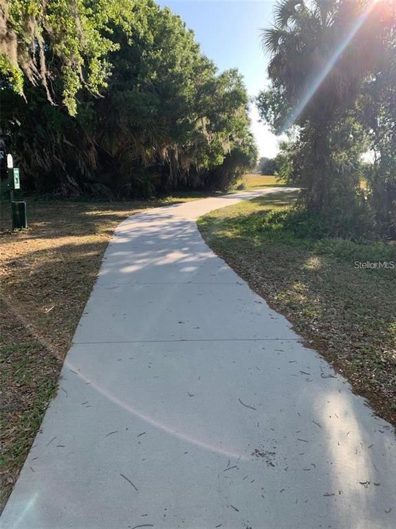 A paved walking path winds through a wooded area with a pet waste station nearby — 16178 TRADING POST ROAD, PUNTA GORDA, FL