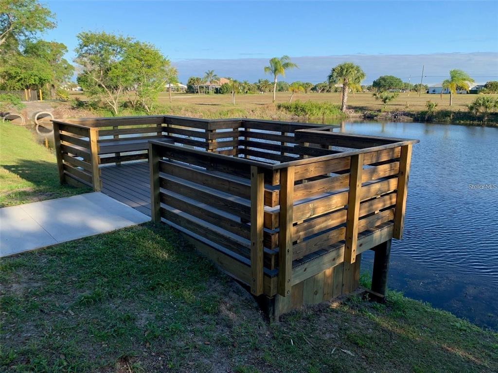 A wooden deck with railings overlooks a pond on a sunny day — 16178 TRADING POST ROAD, PUNTA GORDA, FL