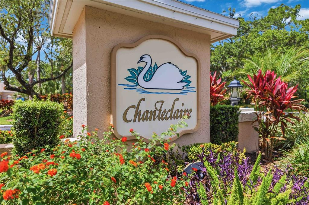 A beige stucco monument sign for Chanteclaire features a swan logo and is surrounded by landscaping — 5526 CHANTECLAIRE UNIT 31, SARASOTA, FL