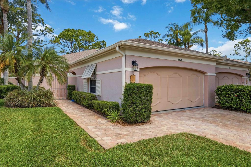 A single-story pink house with a paved driveway, a garage, and a landscaped front yard — 5526 CHANTECLAIRE UNIT 31, SARASOTA, FL