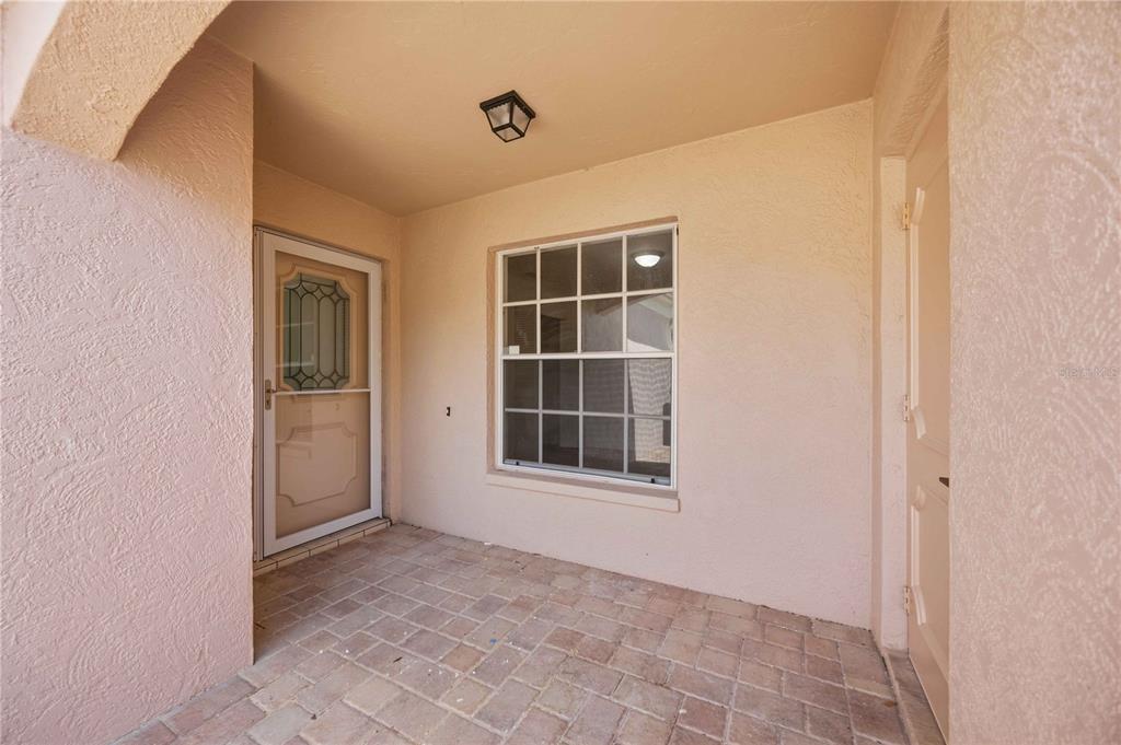 A covered entryway features a brick-paver floor, a storm door, and a single window — 5526 CHANTECLAIRE UNIT 31, SARASOTA, FL
