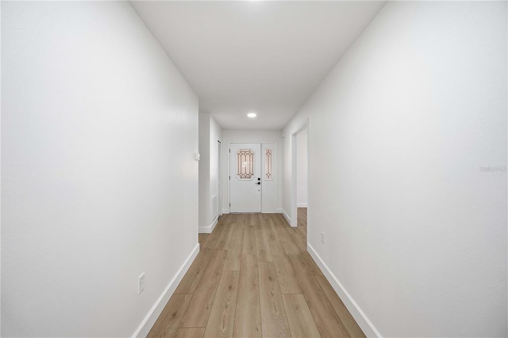 A bright entryway features light wood-look flooring, white walls, and a white front door — 5526 CHANTECLAIRE UNIT 31, SARASOTA, FL