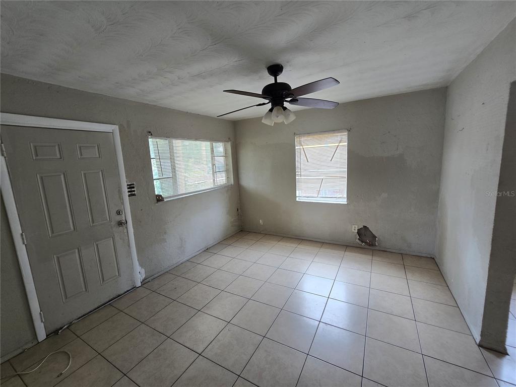 An empty room features tiled floors, a ceiling fan, and damaged walls with two windows — 1511 27TH STREET S, ST PETERSBURG, FL